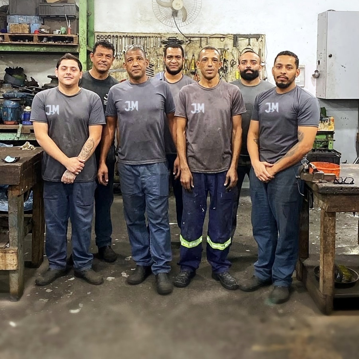 Equipe da JM Eletro Motores uniformizada na oficina de Mogi das Cruzes, entre as bancadas de trabalho